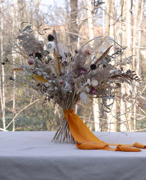 A spring bouquet of dried plants and flowers of pussy willow and feathers on a table in the garden on a sunny day. Easter bouquet in spring.
