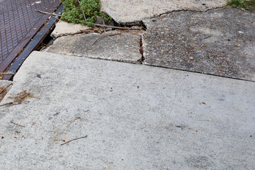 Concrete sidewalk and metal plate, deep cracks and dangerous shifting between sidewalk segments,...