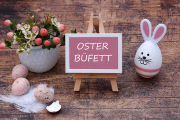 Der Text Osterbüfett ist auf eine Tafel geschrieben mit Ostereiern und Blumen geschmückt.	