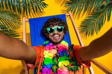 Portrait of satisfied guy with afro hairstyle wear hawaii flower necklace lay on beach make selfie...