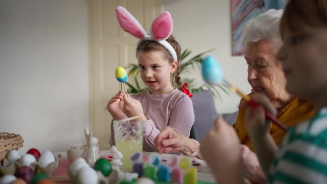 Grandmother with little kids decorating easter eggs at home. Tradition of painting eggs with brush and easter egg dye.