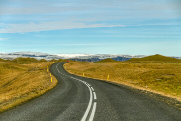 Winding road through barren landscape with snow capped mountains in the distance