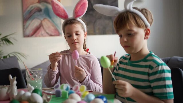 Young kids decorating easter eggs at home. Tradition of painting eggs with brush and easter egg dye.