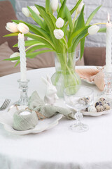 Beautiful table serving for Easter celebration in dining room, candles, glasses, plates with easter eggs and bunny, vase with flowers. Easter table setting.