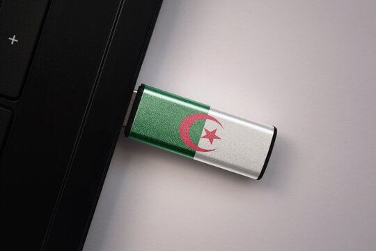 usb flash drive in notebook computer with the national flag of algeria on gray background.