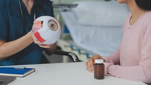 close up of asian female doctor wearing face mask is showing eyeball model and explaining about eyes disease to elder senior man patient in hospital