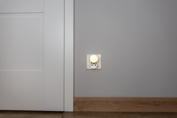Obok drzwi znajduje się gniazdko z zasłonką emitującą światło, co symbolizuje połączenie konceptu elektryczności z ekonomicznymi zagadnieniami, zwłaszcza w kontekście wysokich rachunków za energię ele - obrazy, fototapety, plakaty