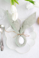 Beautiful table serving for Easter celebration in dining room, plates with easter eggs and bunny, vase with flowers. Easter table setting.