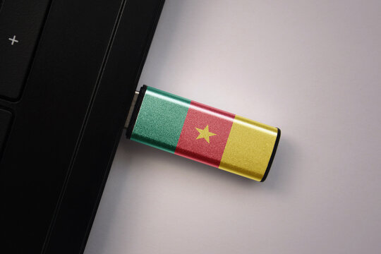 usb flash drive in notebook computer with the national flag of cameroon on gray background.