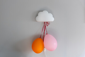 
Dwa kolorowe baloniki przyczepione do lampki dziecięcej w kształcie chmurki symbolizują koncepcję rodziny oraz wydatków związanych z rodzicielstwem i wychowaniem.