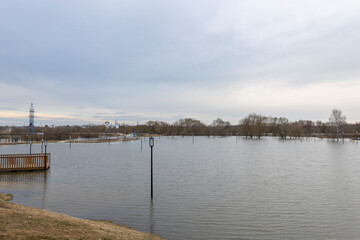 flooded park with paths and sidewalks, early spring flood, river overflowing its banks, environmental pollution, ecology