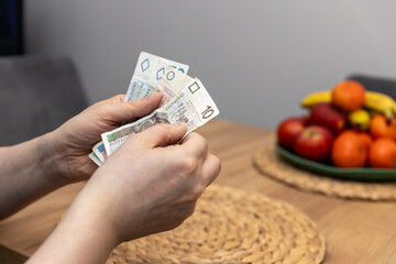 Mężczyzna liczący banknoty o nominałach 20, 50 oraz 10 złotych ilustruje koncepcję znaczących wydatków wobec wysokości wynagrodzenia, z uwzględnieniem wysokiej inflacji oraz rosnących rachunków  - obrazy, fototapety, plakaty