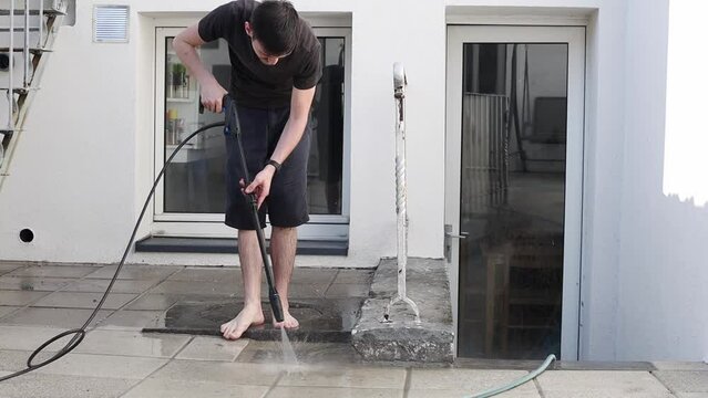 A young man cleans a garden drain in his yard using a Karcher.