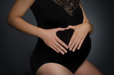 Hands folded with a heart on the belly of a pregnant woman  - obrazy, fototapety, plakaty