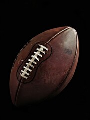 A detailed image of an American football positioned upright against a black background, showcasing the texture of the ball