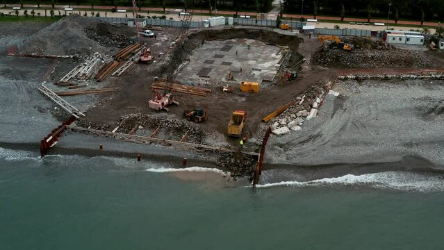 Aerial view of construction site with excavators and dump trucks during earthworks and building foundation construction by the sea side. Construction industry