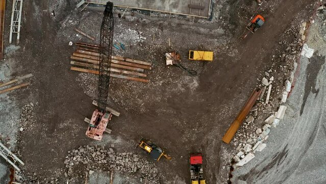 Aerial top down view of construction site with excavators and dump trucks during earthworks and building foundation construction by the sea side. Construction industry