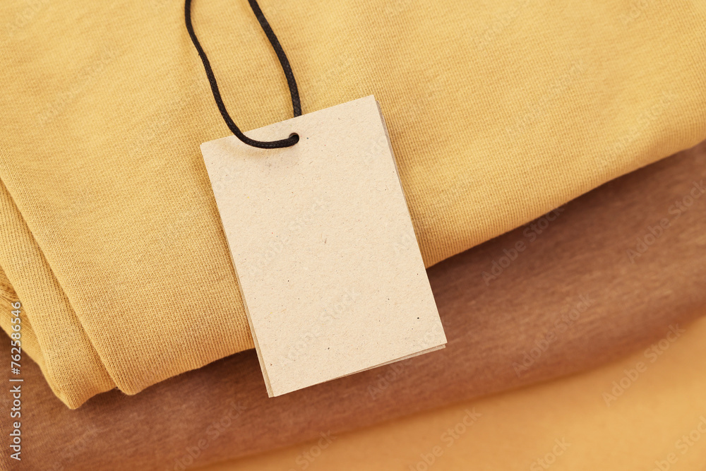 Sticker Garment with cardboard tag on beige background, closeup. Space for text