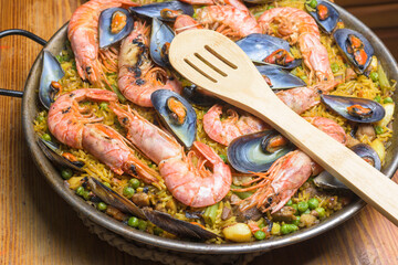 A paella full of seafood, peas, and rice served in a pan with a wooden spoon, typical Spanish cuisine, Majorca, Balearic Islands, Spain