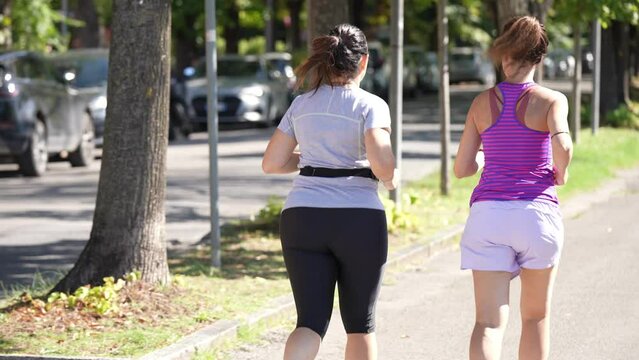 Back view of two females running along a city trail slow motion