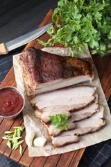 Pieces of baked pork belly served with sauce and parsley on black textured table, above view