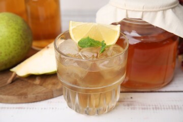 Tasty kombucha and ice cubes in glass on white wooden table, closeup