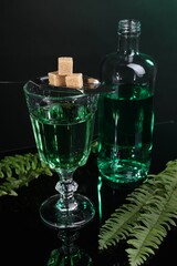 Absinthe, brown sugar, spoon and green leaves on mirror table. Alcoholic drink