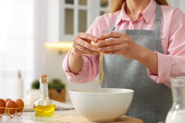 Making bread. Woman putting raw egg into bowl at white table in kitchen, closeup