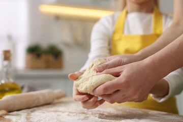 Making bread. Mother and her daughter kneading dough at wooden table in kitchen, closeup