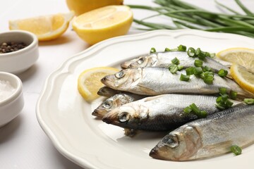 Fresh raw sprats, green onion, spices and cut lemon on white table, closeup