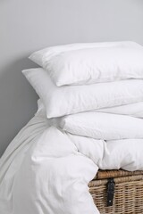 Fototapeta na wymiar Soft pillows and duvet on wicker trunk near grey wall indoors
