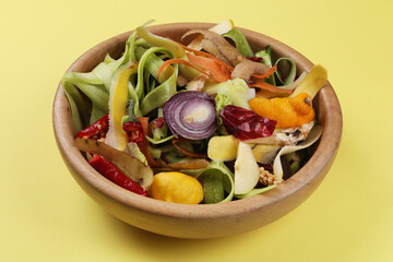 Peels of fresh vegetables in bowl on yellow background