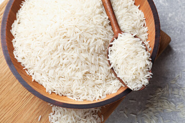Raw basmati rice in bowl and spoon on grey table, top view