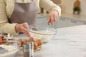 Woman making dough with whisk in bowl at light marble table, closeup. Space for text