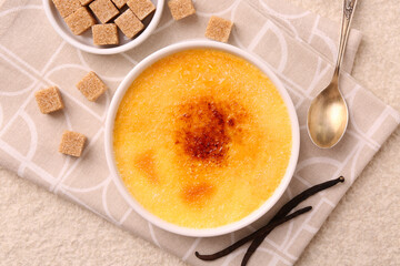 Delicious creme brulee in bowl, vanilla pods, sugar cubes and spoon on light textured table, top view