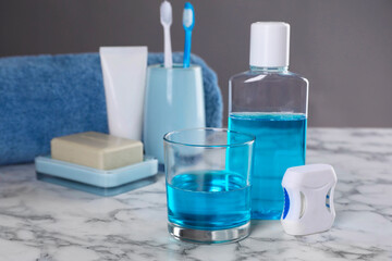 Fresh mouthwash in bottle, glass and dental floss on white marble table. Space for text