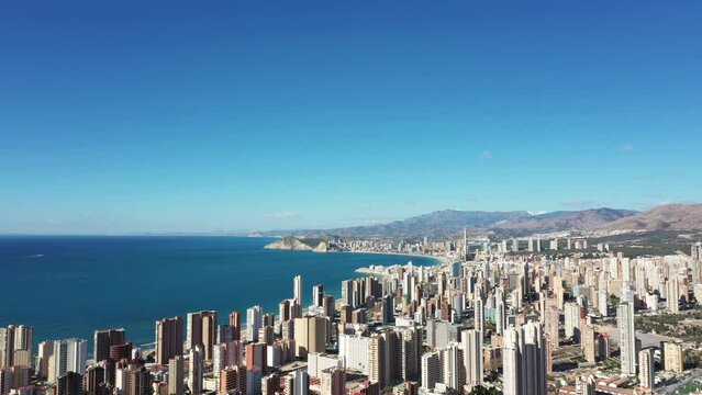 Aerial drone footage of the town of Benidorm in Spain showing the beach front as viewed by the hillside on a clear sunny summers day,