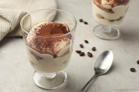 Delicious tiramisu in glass, spoon and scattered coffee beans on light table