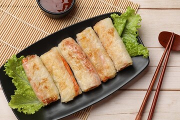 Delicious fried spring rolls, sauce and chopsticks on light wooden table, flat lay