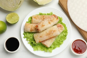 Delicious fried spring rolls served on white marble table, flat lay