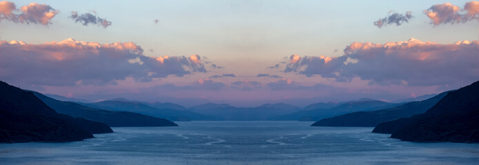 Beautiful panorama of the sea and mountains with blue water and purple clouds on the sky at the sunset.