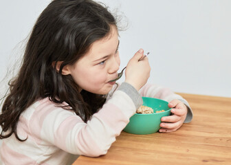 young girl in pink striped pajamas eating oatmeal for breakfast