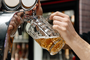 bartender pours light beer into large beer mug for customer at bar, close-up view of hand holding...