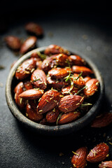 Close up of roasted almonds with rosemary in a bowl on a dark background - 762611370