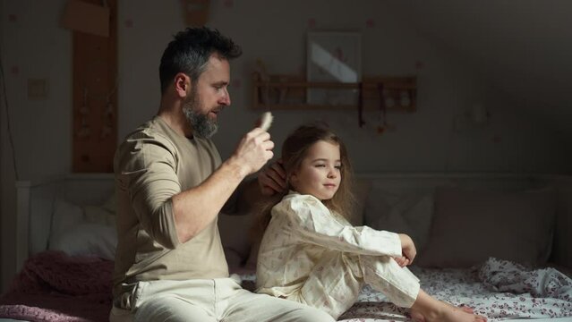 Father combing and braiding daughter's hair as part of bedtime routine. Single dad taking care of his daughter's hairstyle.