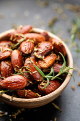 Close up of roasted almonds with rosemary in a wooden bowl on a grey background