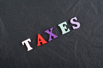 TAXES word on black board background composed from colorful abc alphabet block wooden letters, copy...