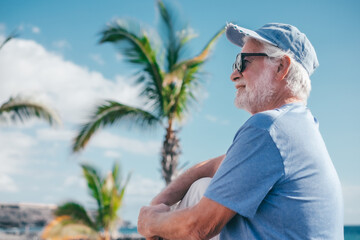 Handsome smiling senior bearded man sitting outdoors face the sea enjoying sunny day, travel,...