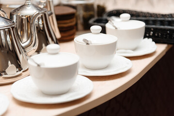 Fototapeta na wymiar three small white tea cups with lids and spoons on saucers on counter, tableware for cafes, restaurant equipment