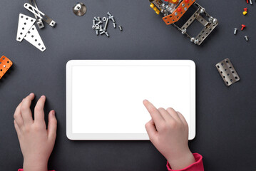 Tablet mockup on work desk. Child's hands touch isolated display. Top view, flat lay desk composition with small metal parts and screws